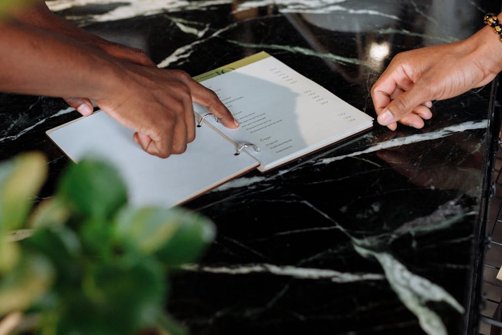 Hands pointing at menu on black marble counter inside a shop.